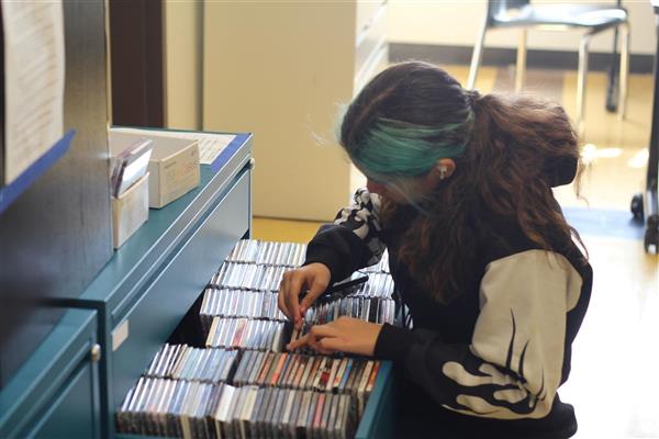 A student sits in front of an open drawer full of CDs. They are holding a CD in their hand and looking down at the many musical options. They are about to pick something awesome to play on KECG.